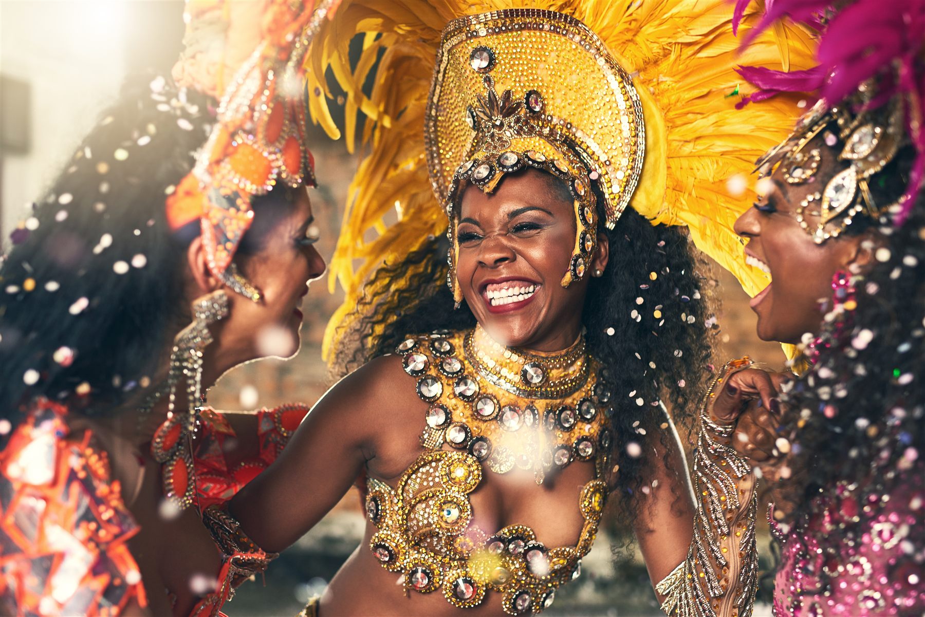 Carnival masqueraders laughing together in bright yellow costume details.